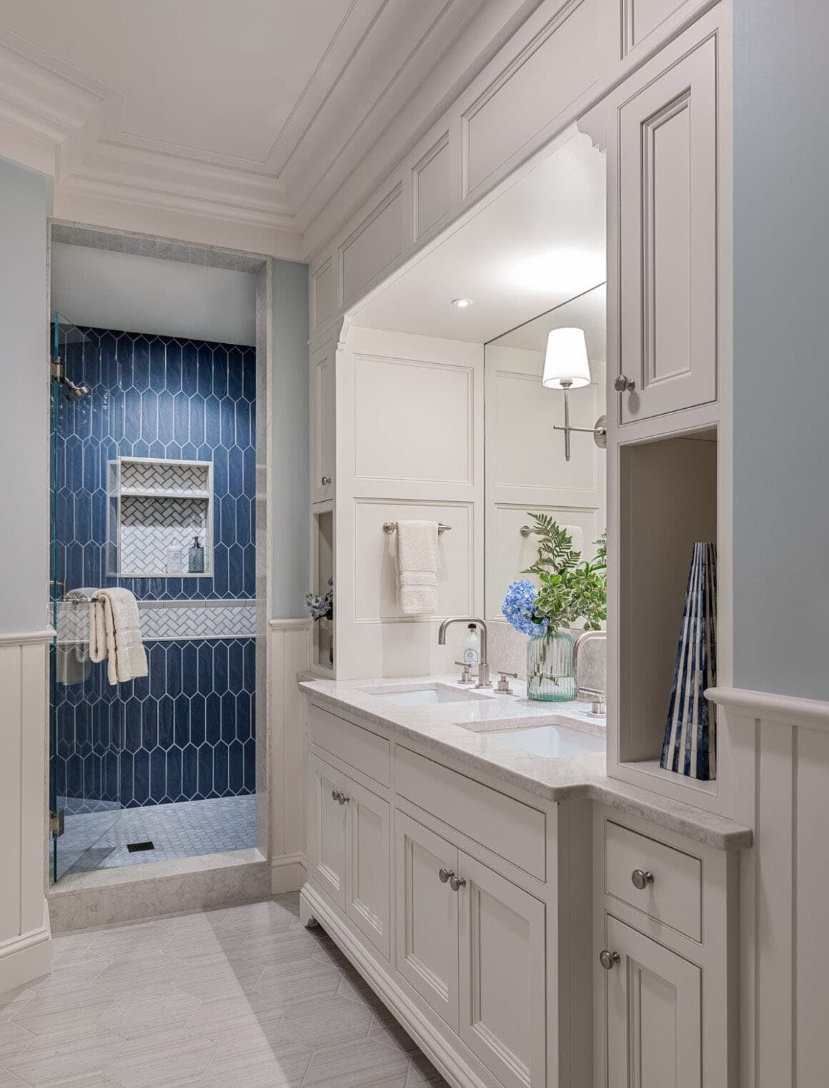 Blue beadboard bathroom with double vanity and honeycomb tile shower visible through doorway