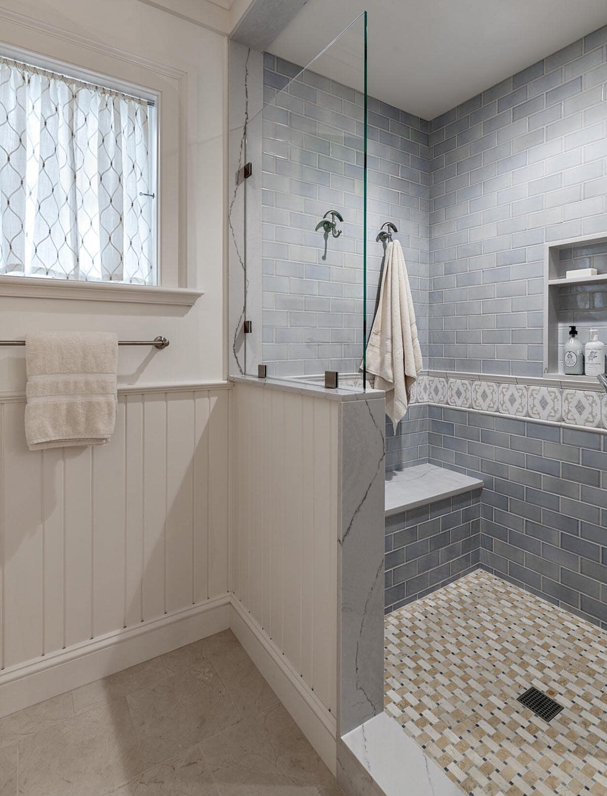 Walk-in shower with blue subway tile, built-in bench, and mosaic tile floor