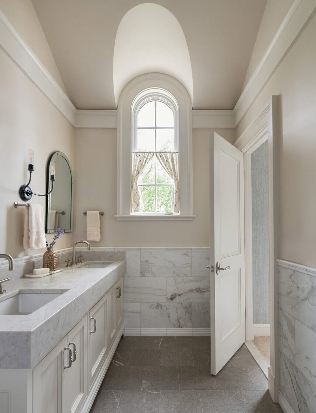 Powder room with arched alcove ceiling, marble wainscoting, and arched window