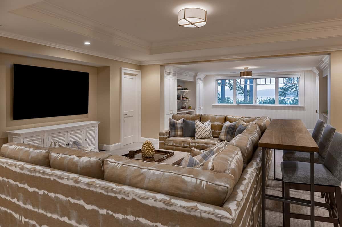 Lower-level lounge with patterned sectional, wall-mounted TV, and lake-view window beyond