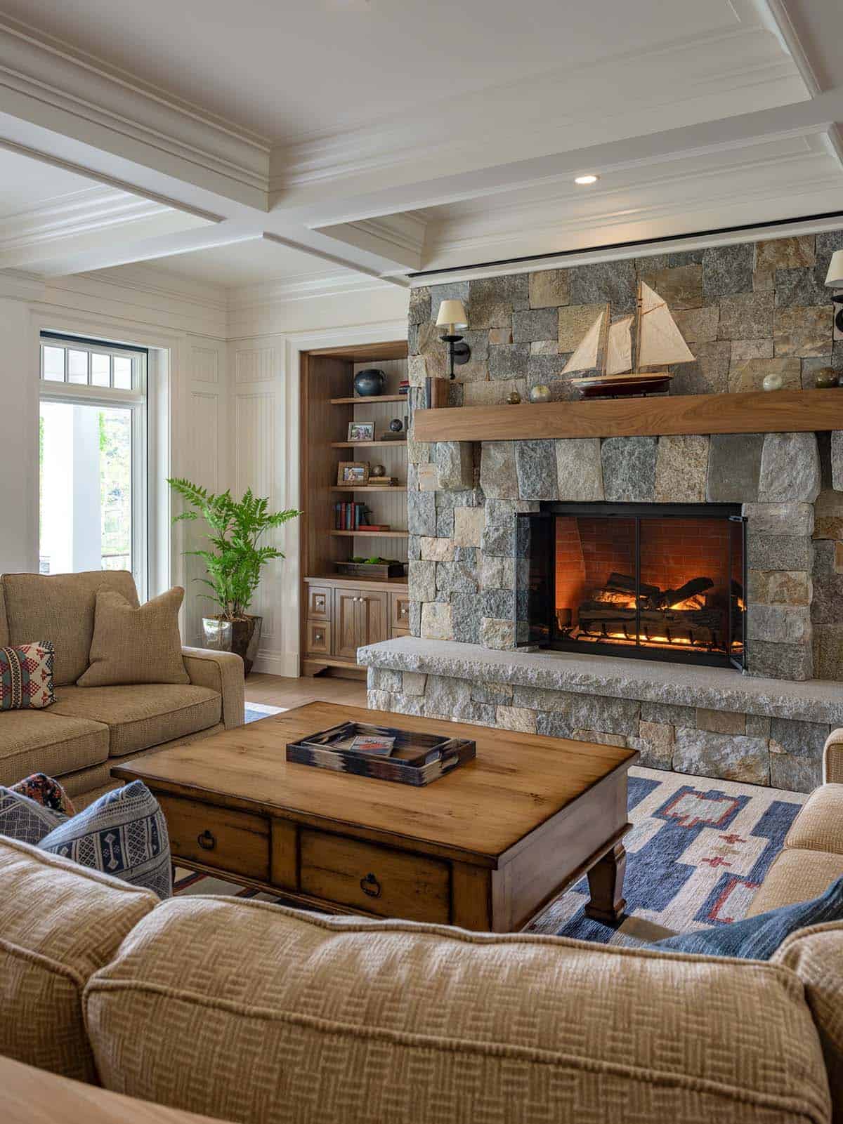 Living room with stone fireplace, wood mantel, model sailboat, and built-in shelving