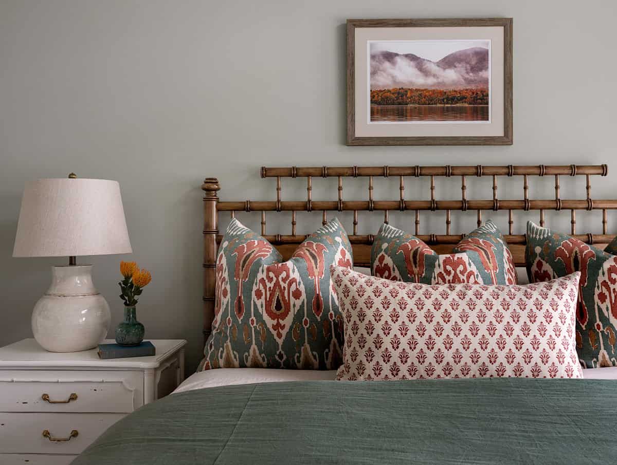 Bed with bamboo-style headboard, ikat pillows, and framed mountain landscape photo