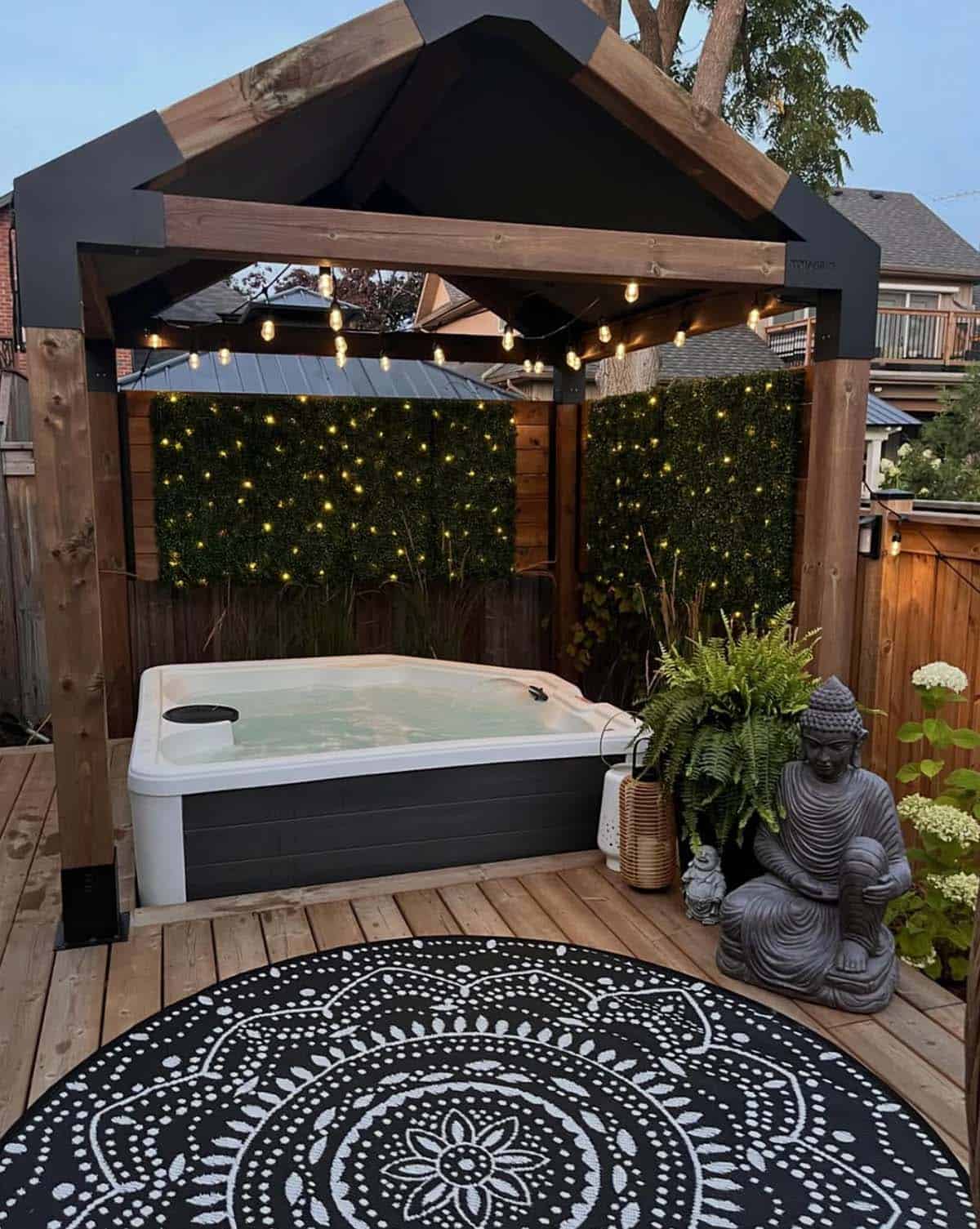 A private, pergola-covered hot tub deck with artificial hedge panels, string lights, and blooming hydrangeas