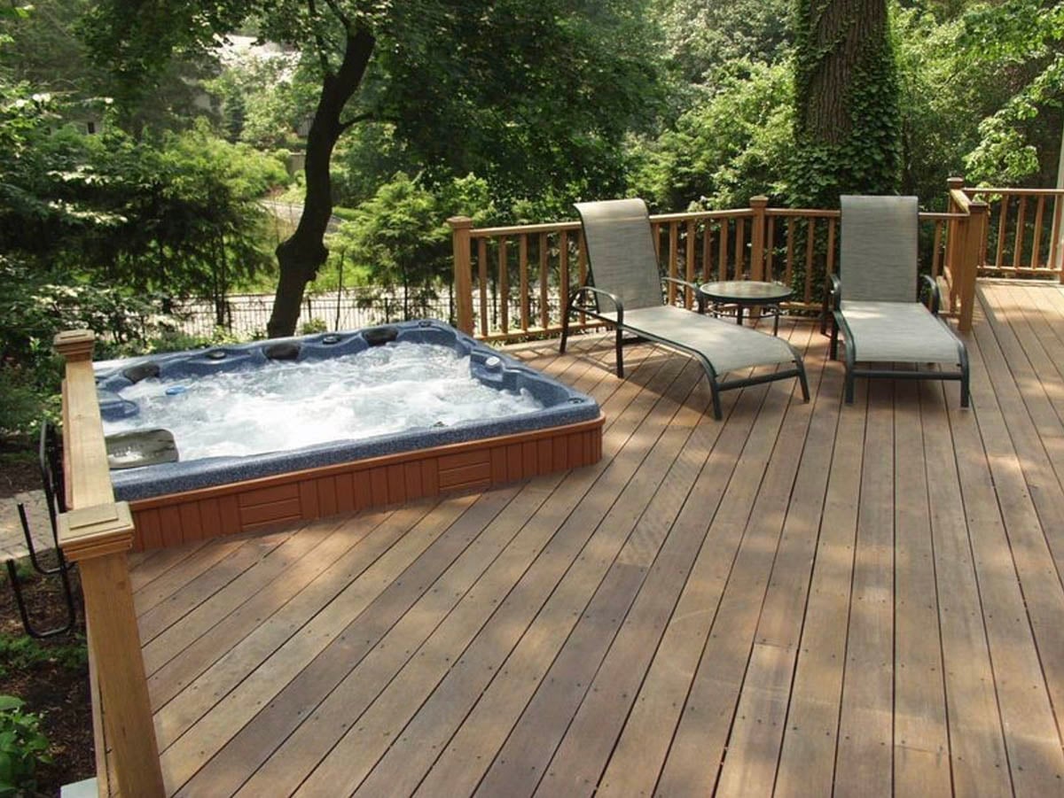 A wood deck hot tub surrounded by lounge chairs and tall trees in a wooded New York backyard