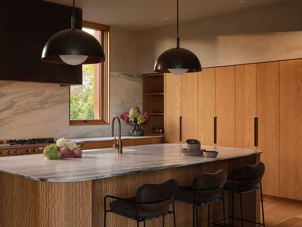 Kitchen with marble island, oak cabinetry, marble backsplash, and black dome pendants