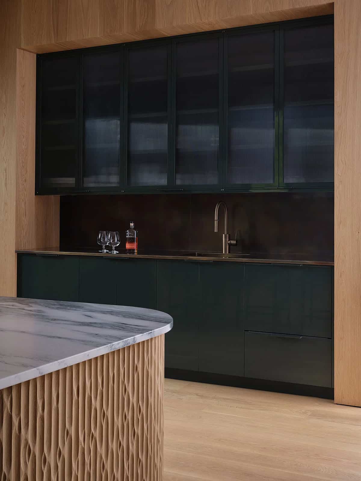 Dark green bar cabinetry with ribbed oak island, marble countertop, and brass fixtures