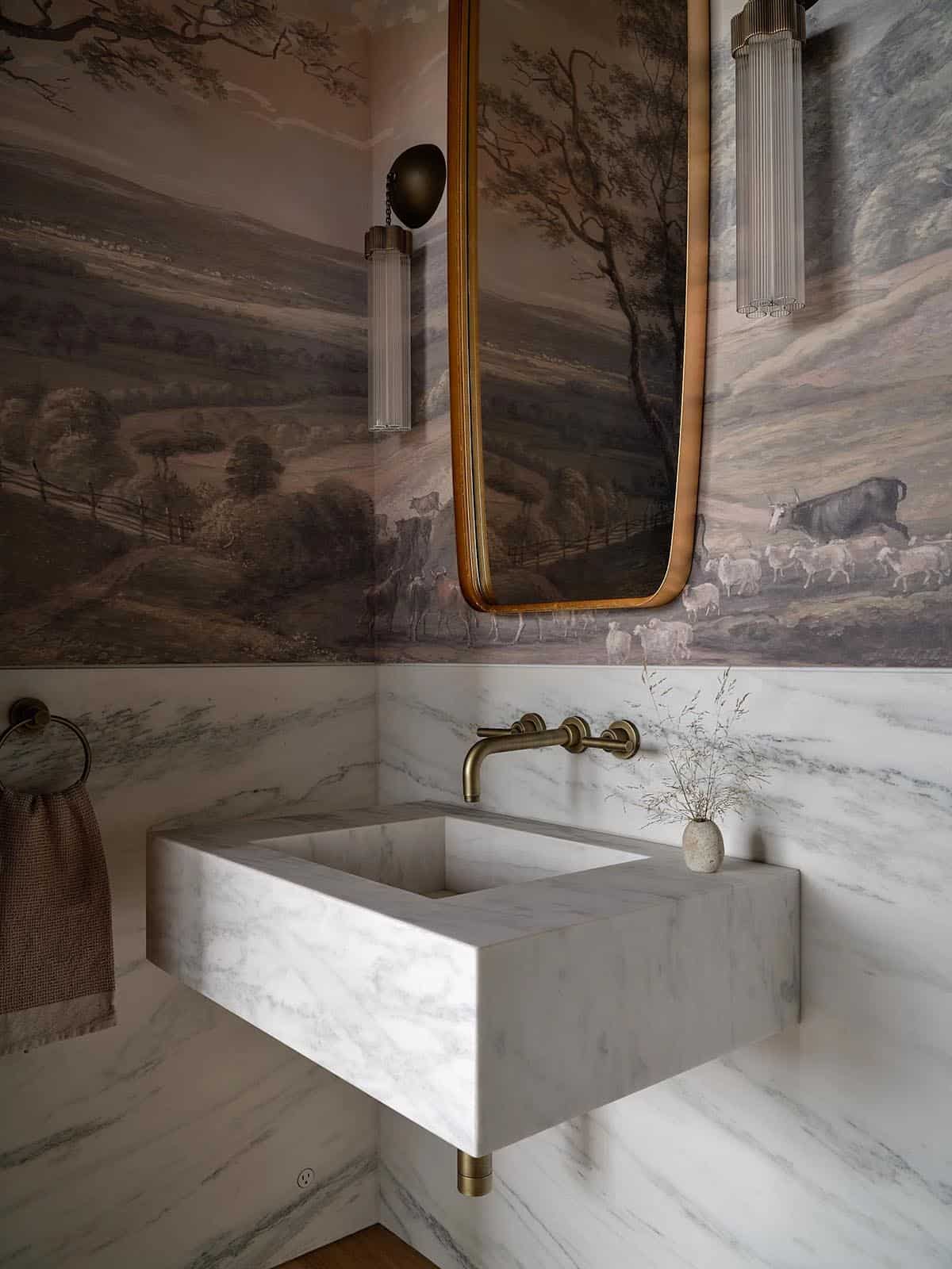 Powder room with scenic pastoral wallpaper mural, marble sink, and brass wall-mount faucet