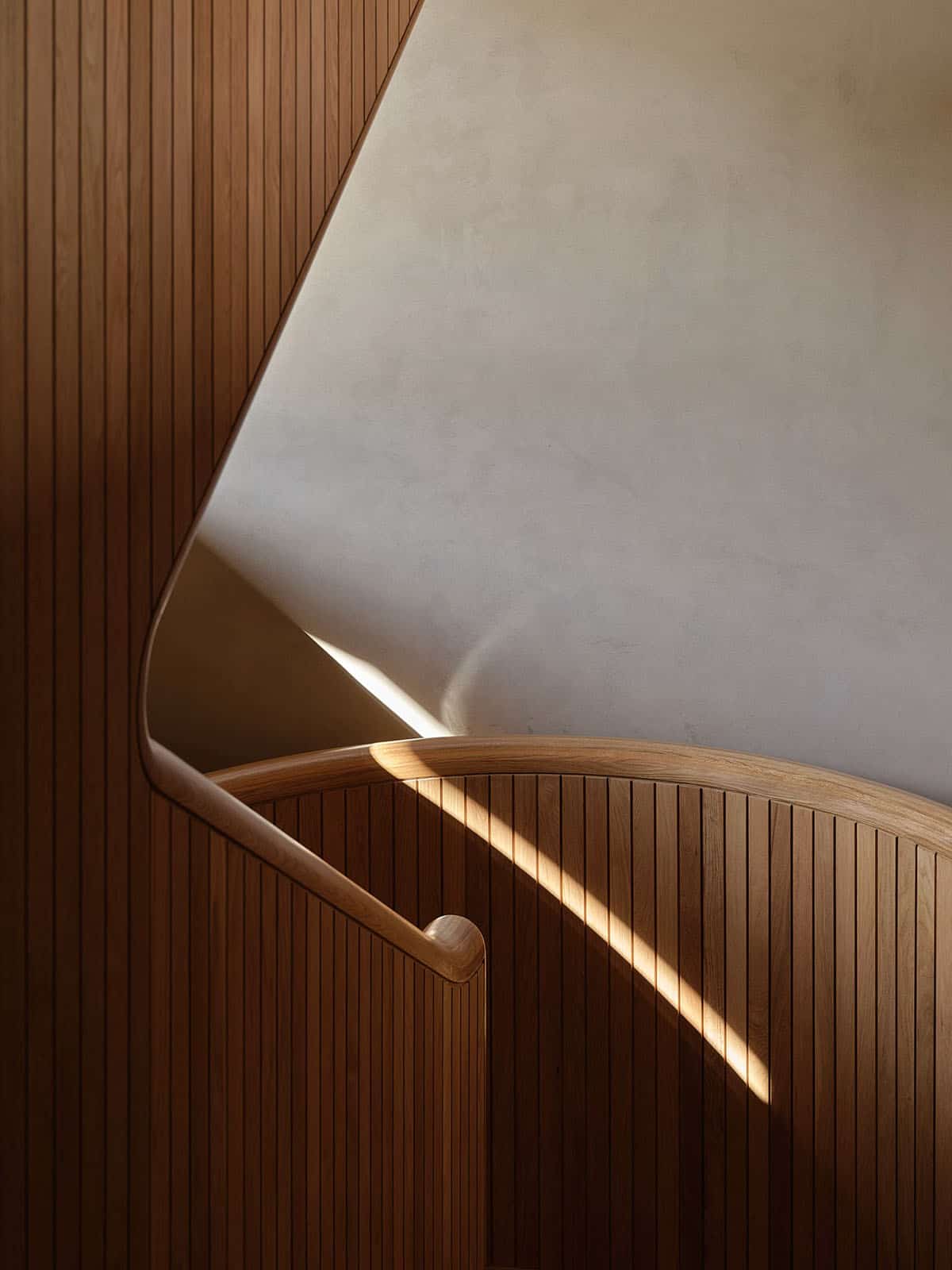 Detail of curved oak handrail and vertical wood slat balustrade with raking sunlight