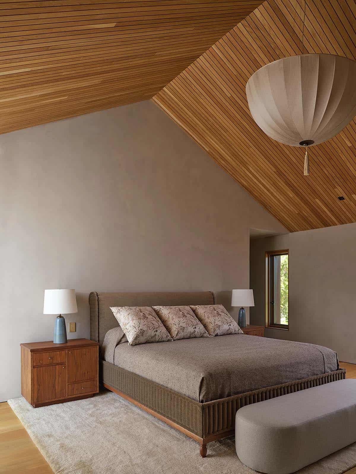 Primary bedroom with angled cedar ceiling, fabric globe pendant, and warm plaster walls