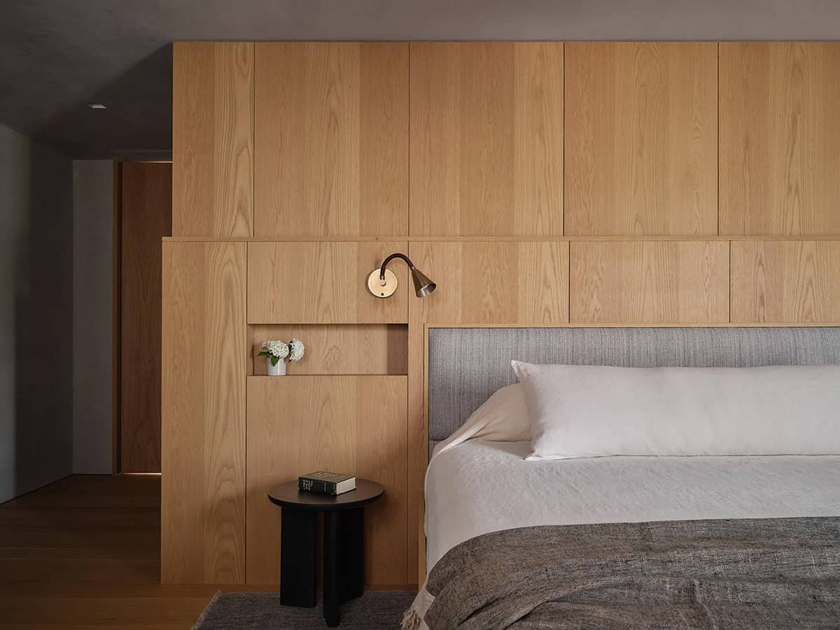 Guest bedroom with full-height oak headboard wall, integrated reading sconce, and built-in niche