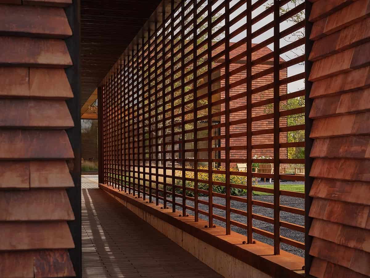 Covered walkway with floor-to-ceiling Corten steel grid screen filtering garden views