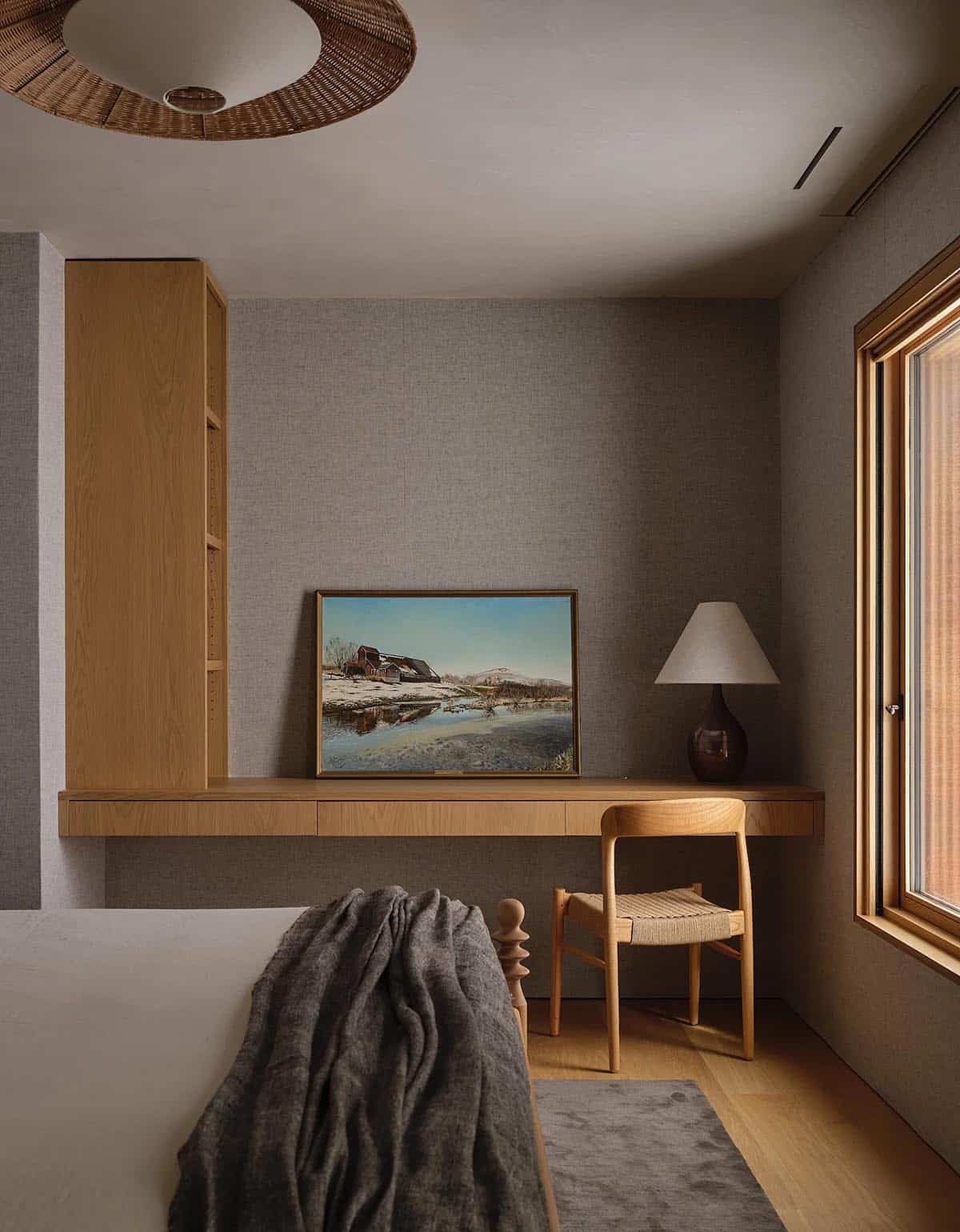 Guest bedroom with floating oak desk, woven chair, Vermont landscape painting, and linen wallcovering