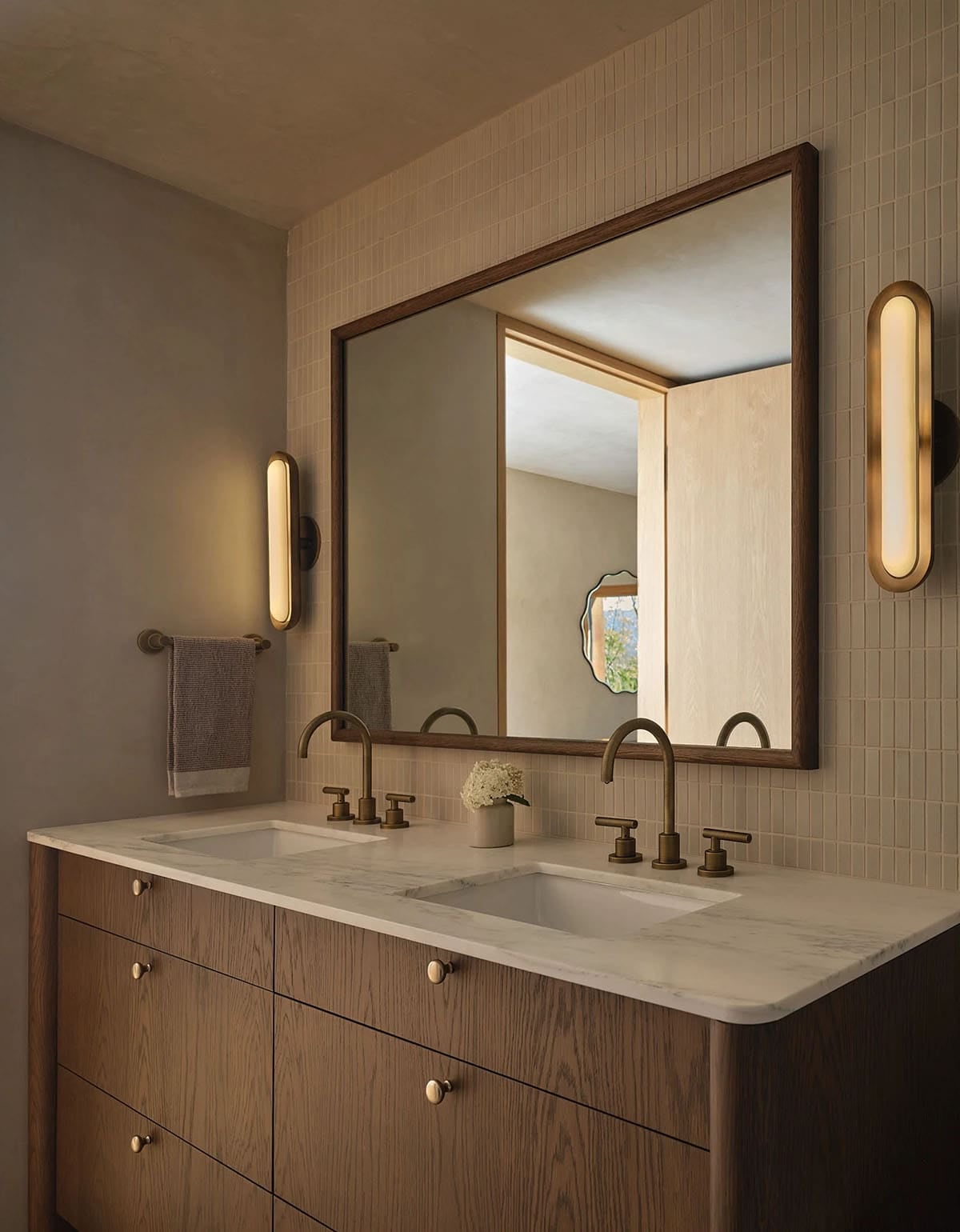 Guest bathroom double vanity with walnut-framed mirror, marble countertop, and pill-shaped brass sconces