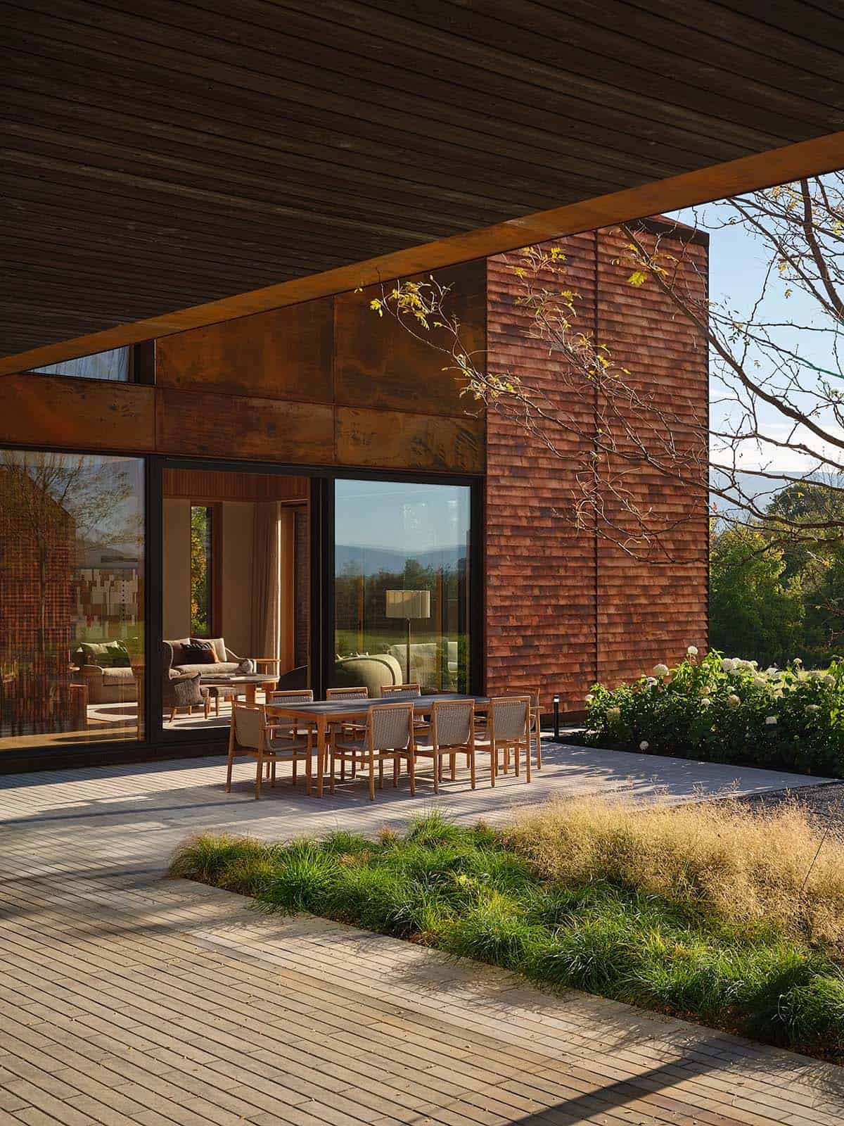 Outdoor dining terrace under Corten steel overhang with teak table set and ornamental grasses