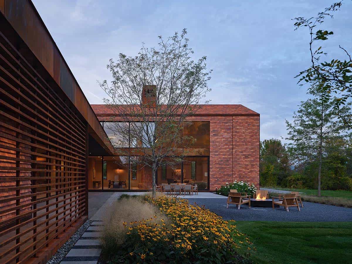 Dusk courtyard view with lit fire pit, black-eyed Susans, and cedar-clad gabled wing