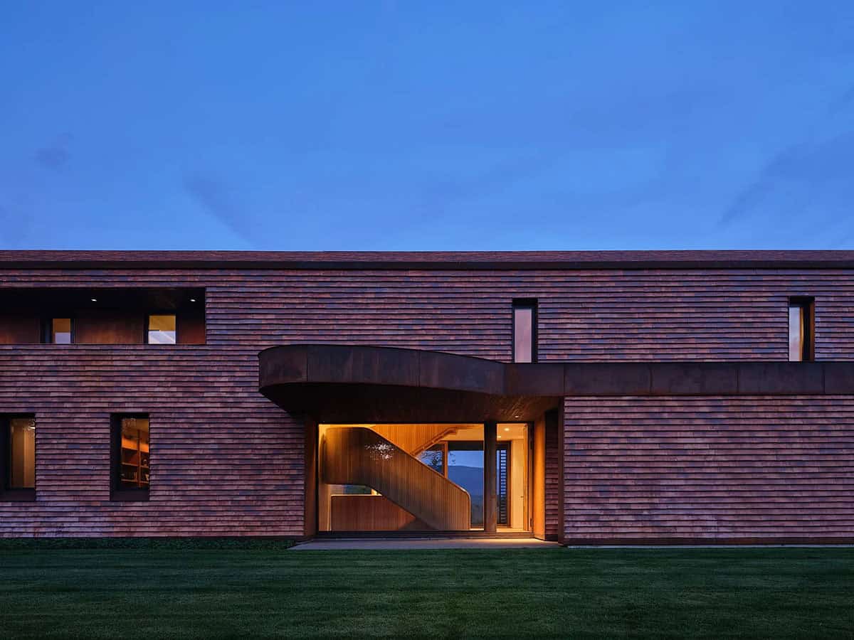 Front facade at dusk with glowing entry portal revealing curved oak staircase beyond