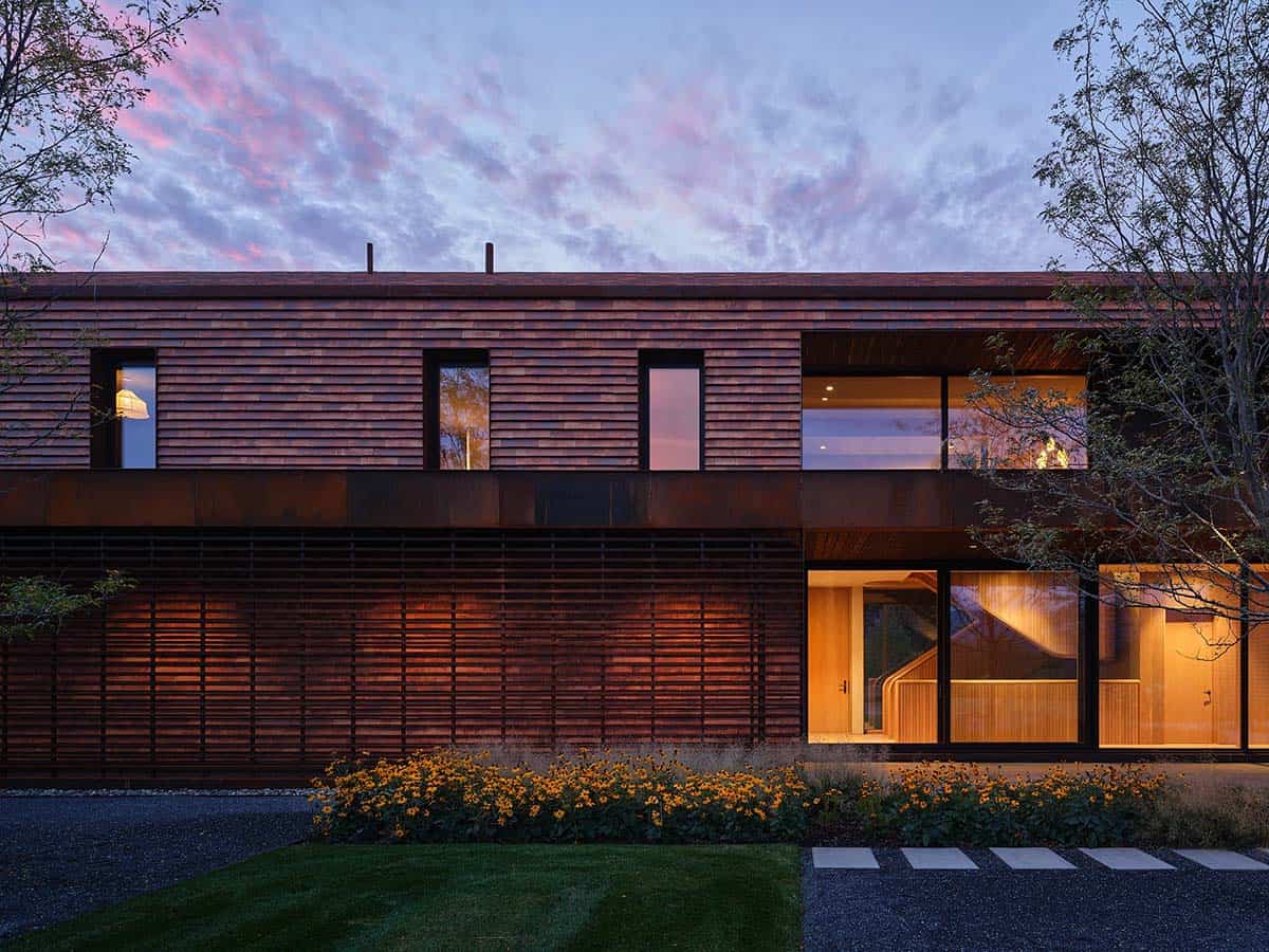 Twilight exterior with Corten steel horizontal louvers, lit interior, and pink-streaked sky