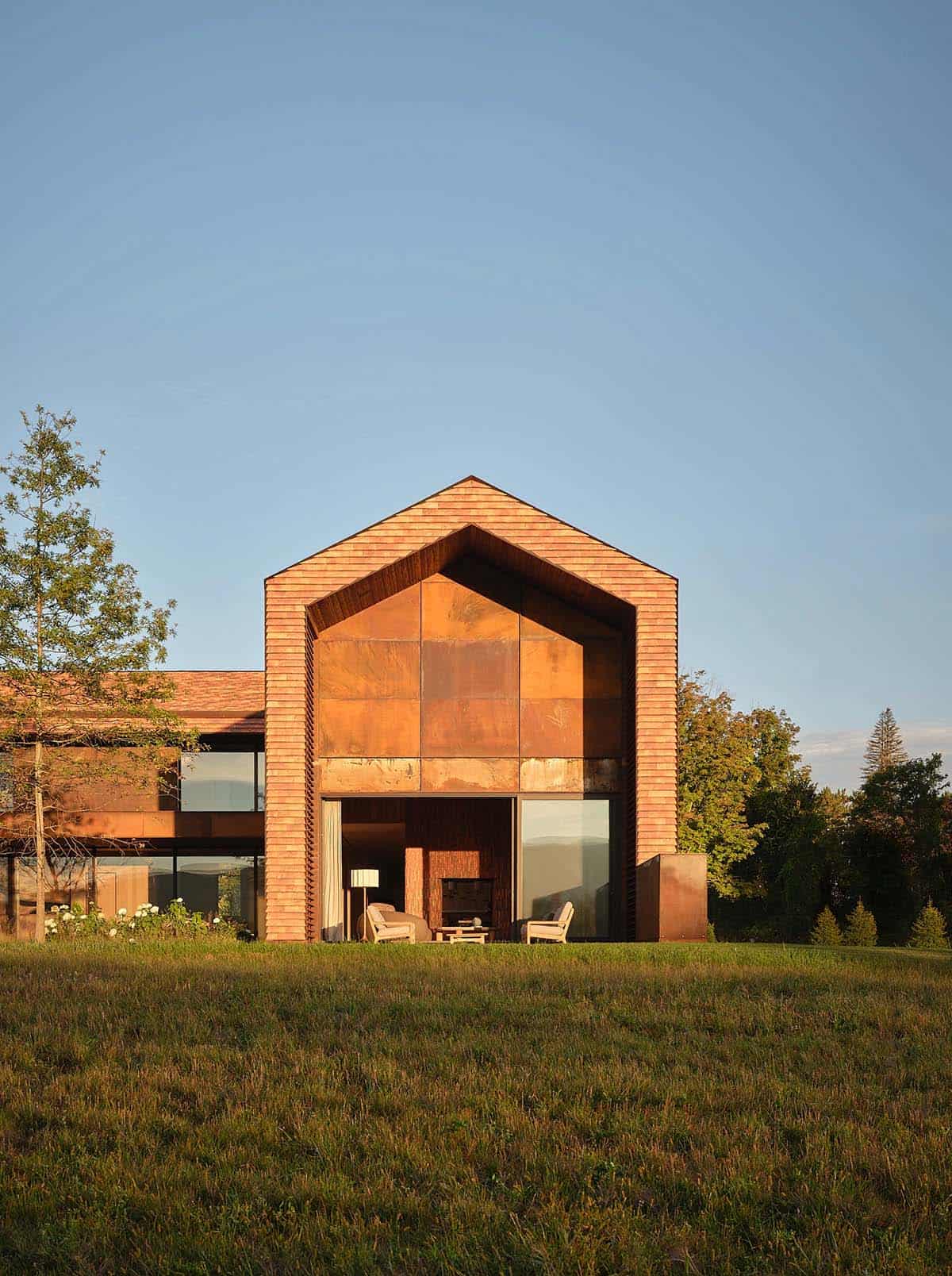 Cedar-clad gabled guest pavilion with Corten steel gable face and floor-to-ceiling glazing at golden hour