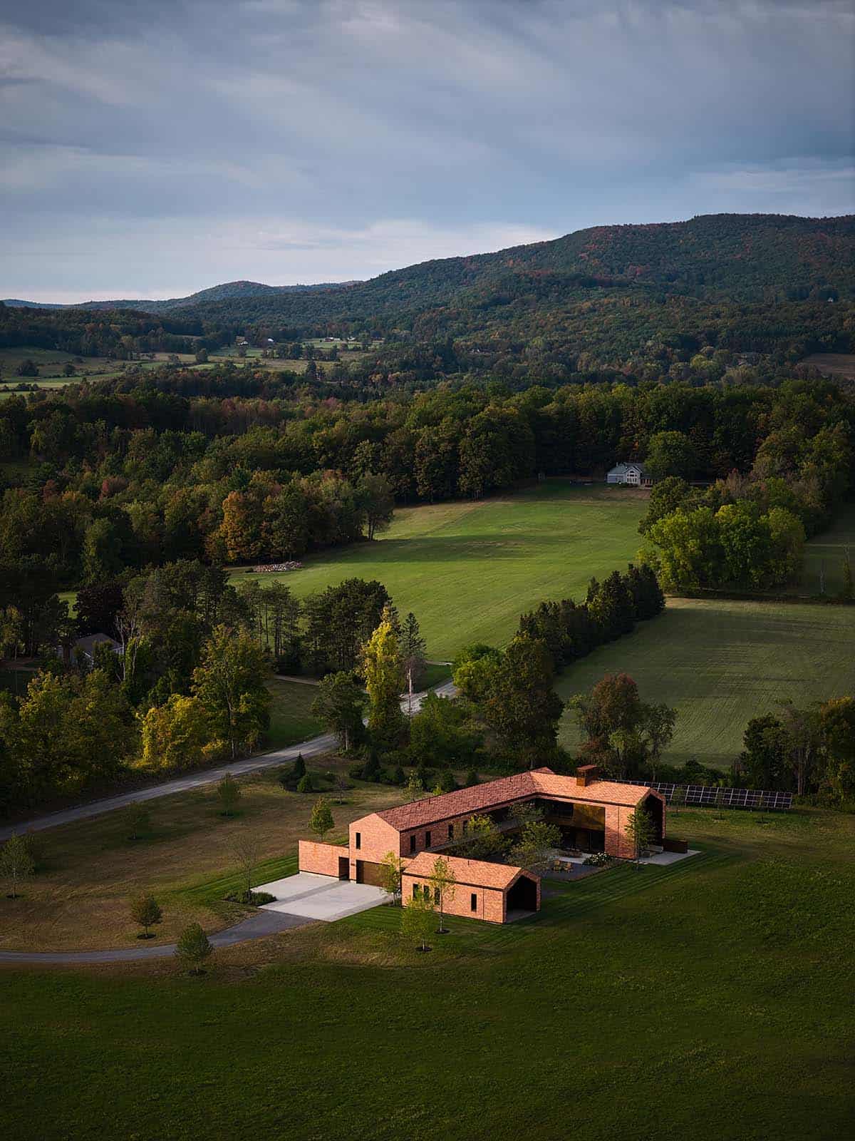 Aerial drone view of cedar-shingled compound nestled in southern Vermont farmland with mountain backdrop