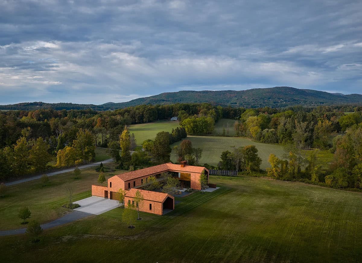 Aerial view of L-shaped cedar shingle compound set within rolling Vermont fields and autumn foliage