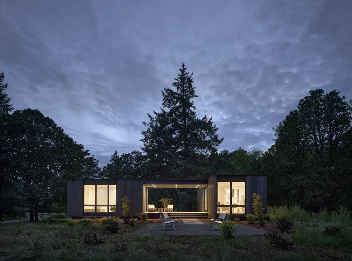 Dark metal-clad house with open breezeway glowing at dusk