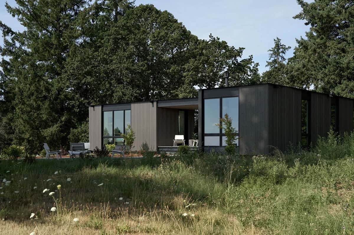 Dark corrugated metal house with covered porch in tall grass