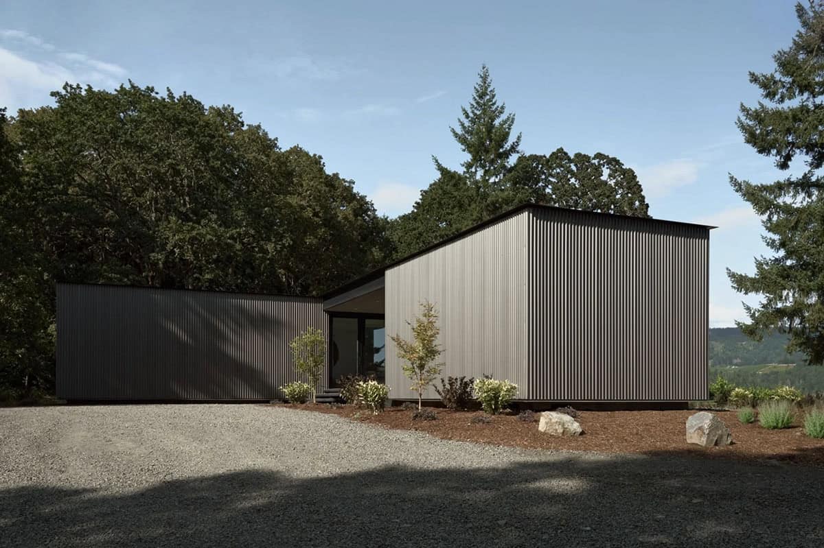Angular corrugated metal house exterior against a forested hillside