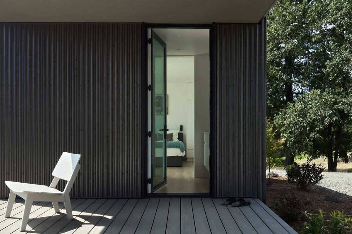 Open glass door leading from deck into bedroom with metal siding