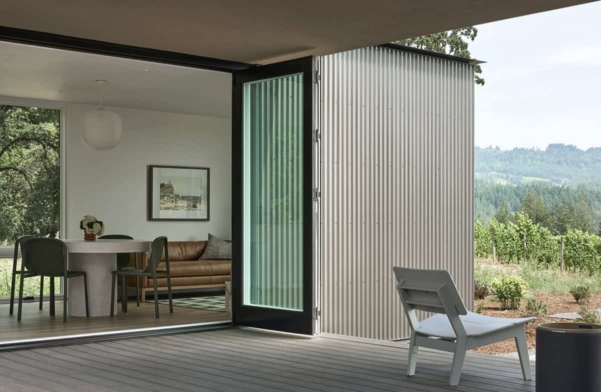 Open pivot door connecting living room to deck with vineyard beyond