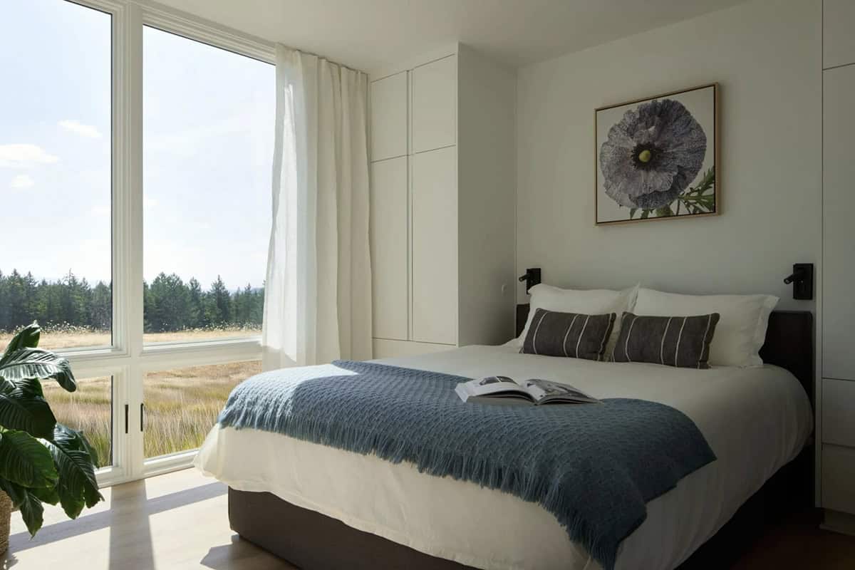 Bedroom with floor-to-ceiling window overlooking open meadow