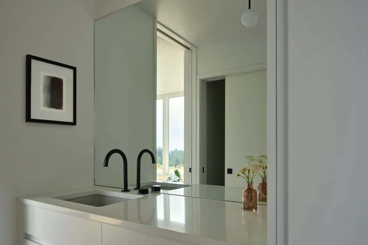 Bathroom vanity with black fixtures reflecting hallway in mirror