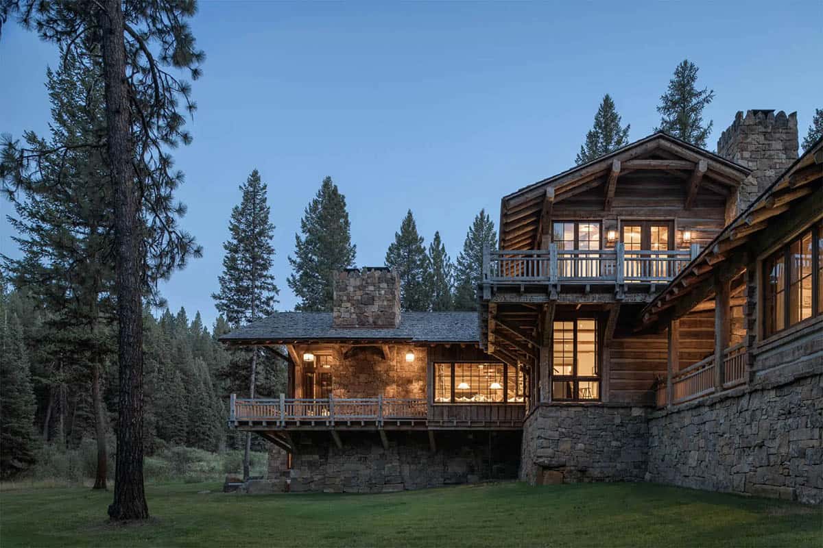 Cabin exterior at twilight with stone chimney, log walls, and wraparound deck