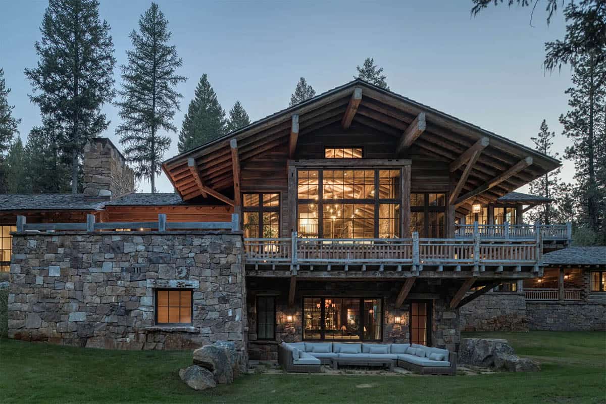 Rustic cabin great room exterior with timber gable, stone base, and lit interior