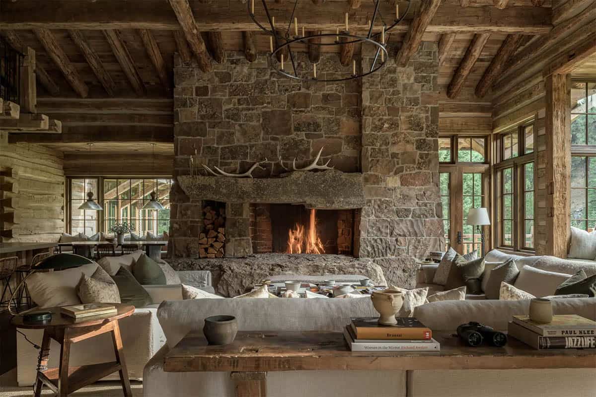 Great room with massive stone fireplace, log beams, and linen sofas