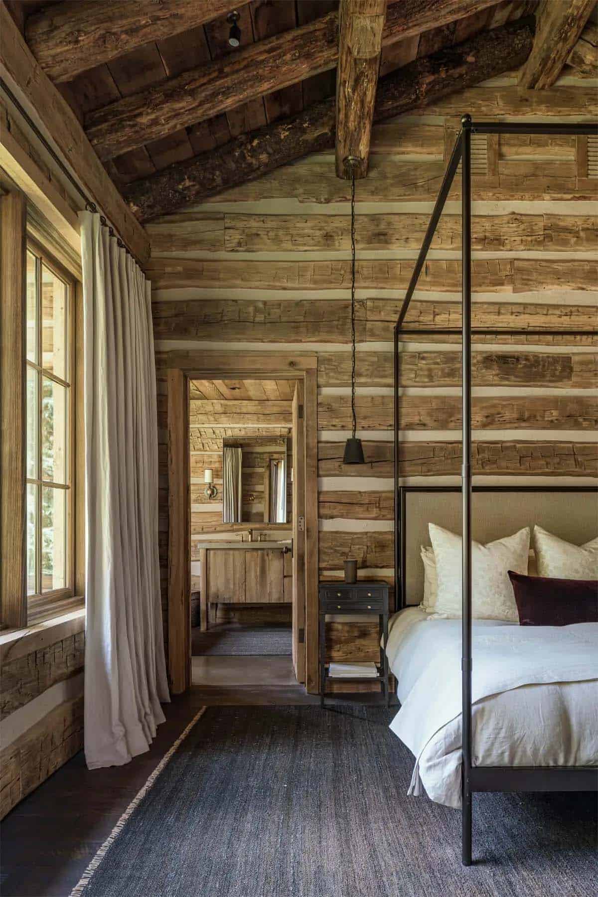 Rustic log bedroom with canopy bed and view into wood-paneled bathroom