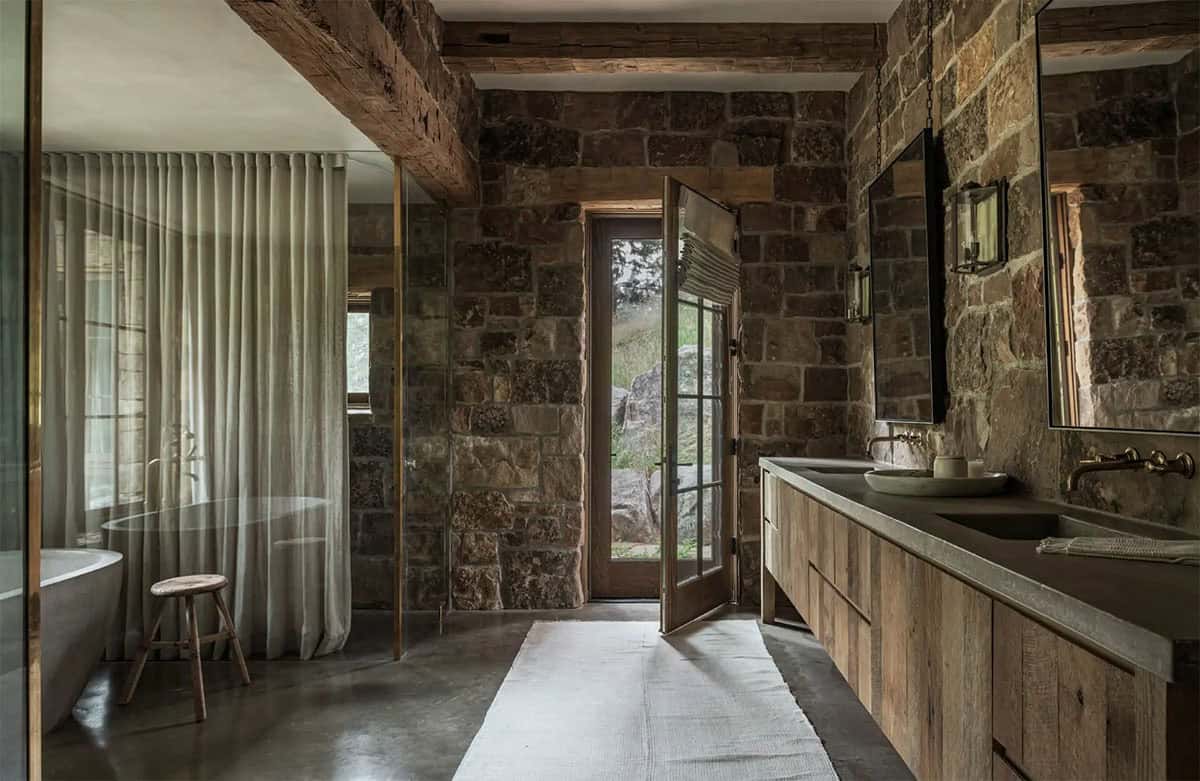 Stone-walled bathroom with freestanding tub, glass partition, and French door