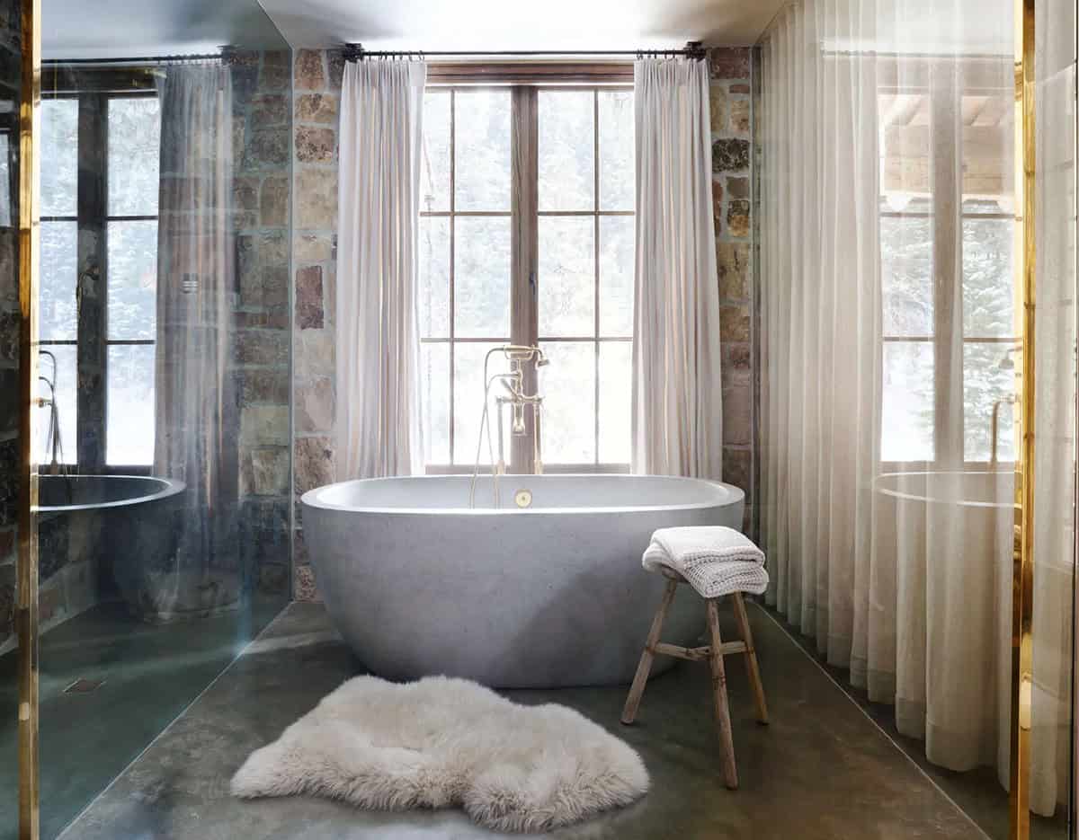 Concrete soaking tub before curtained window with brass fixtures