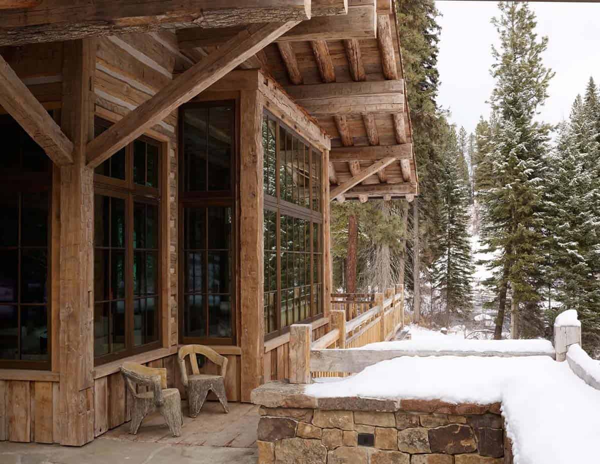 Snow-covered porch with timber posts and rustic wood chairs