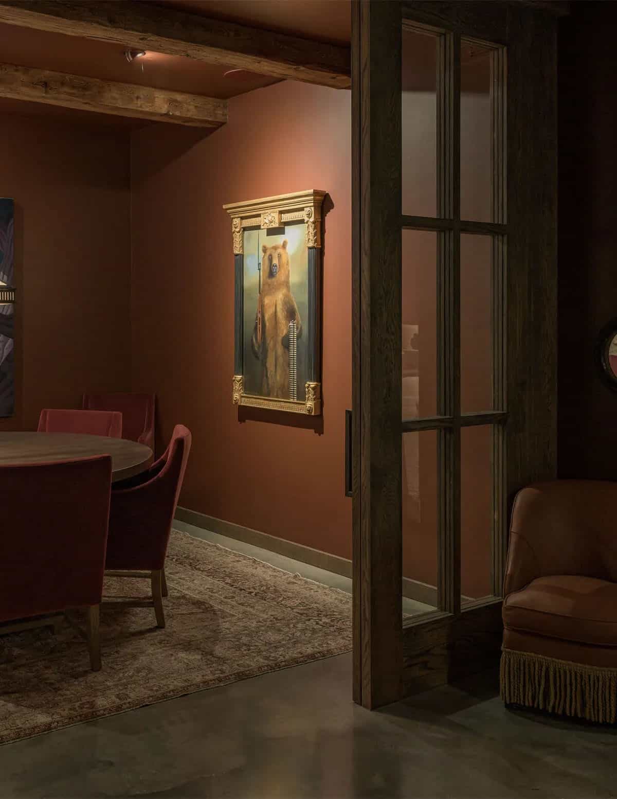 Moody den with red velvet chairs and framed bear painting on rust-colored wall