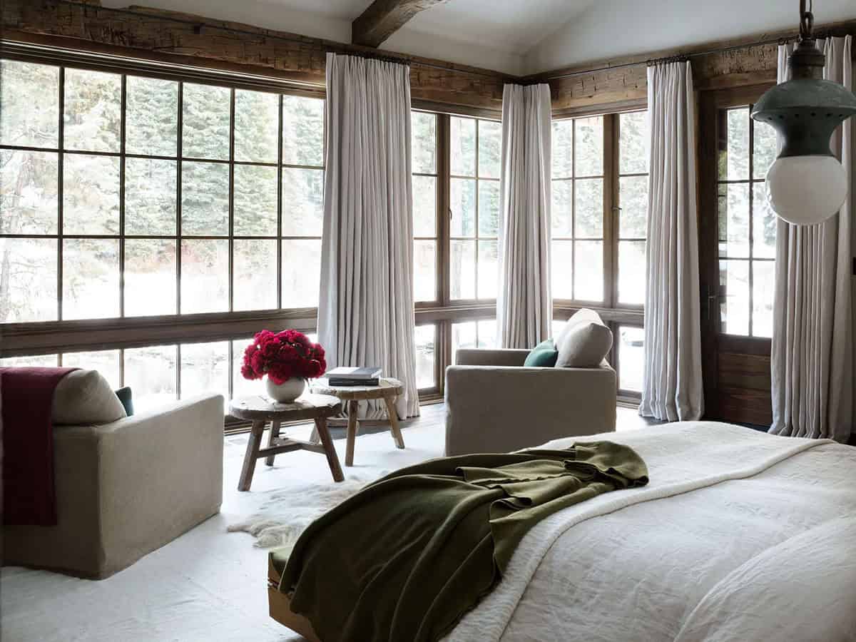 Bright bedroom corner with floor-to-ceiling windows overlooking snowy forest