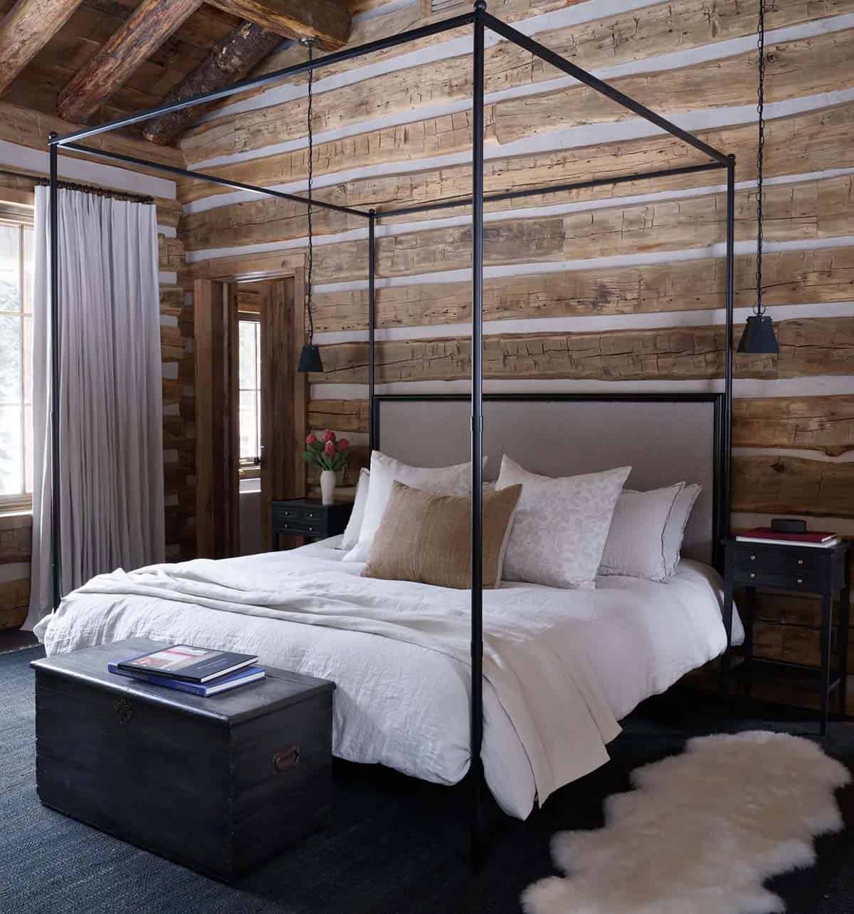 Log cabin bedroom with black canopy bed and antique wooden trunk