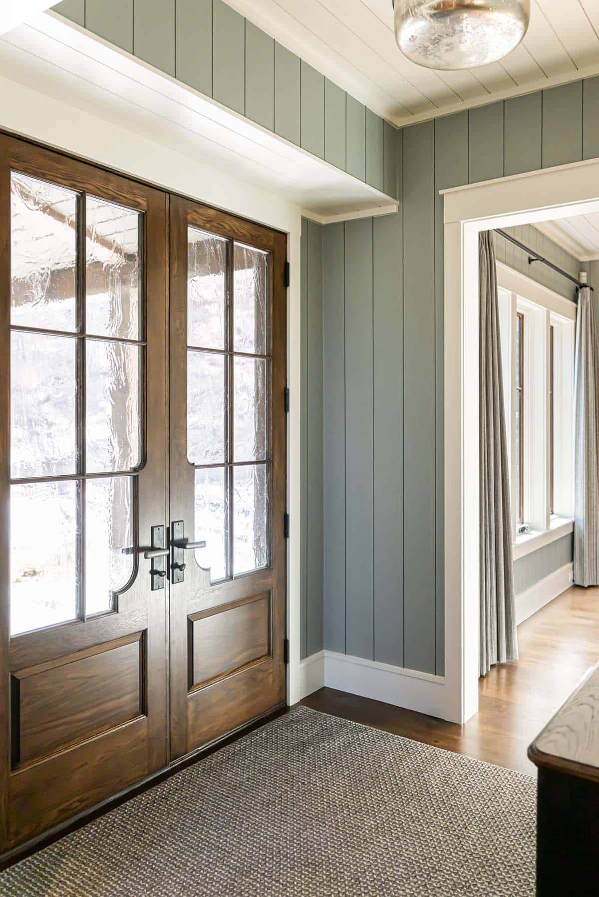 Entryway with glass front doors and sage green shiplap walls