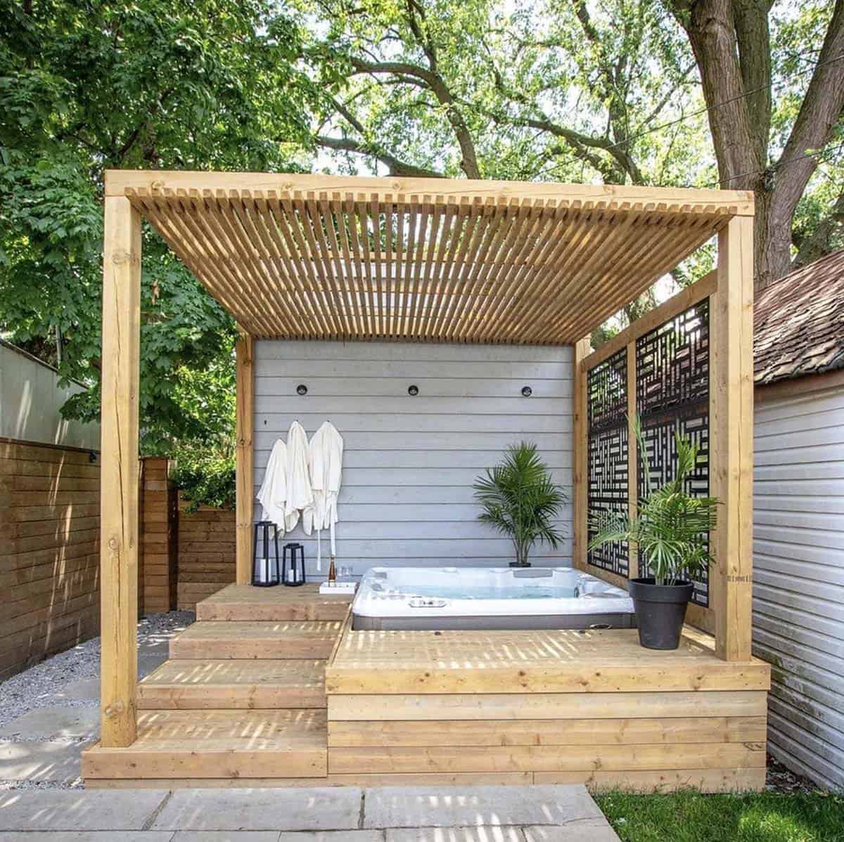 A raised wood deck hot tub under a slatted pergola roof with a decorative privacy screen and hanging robes