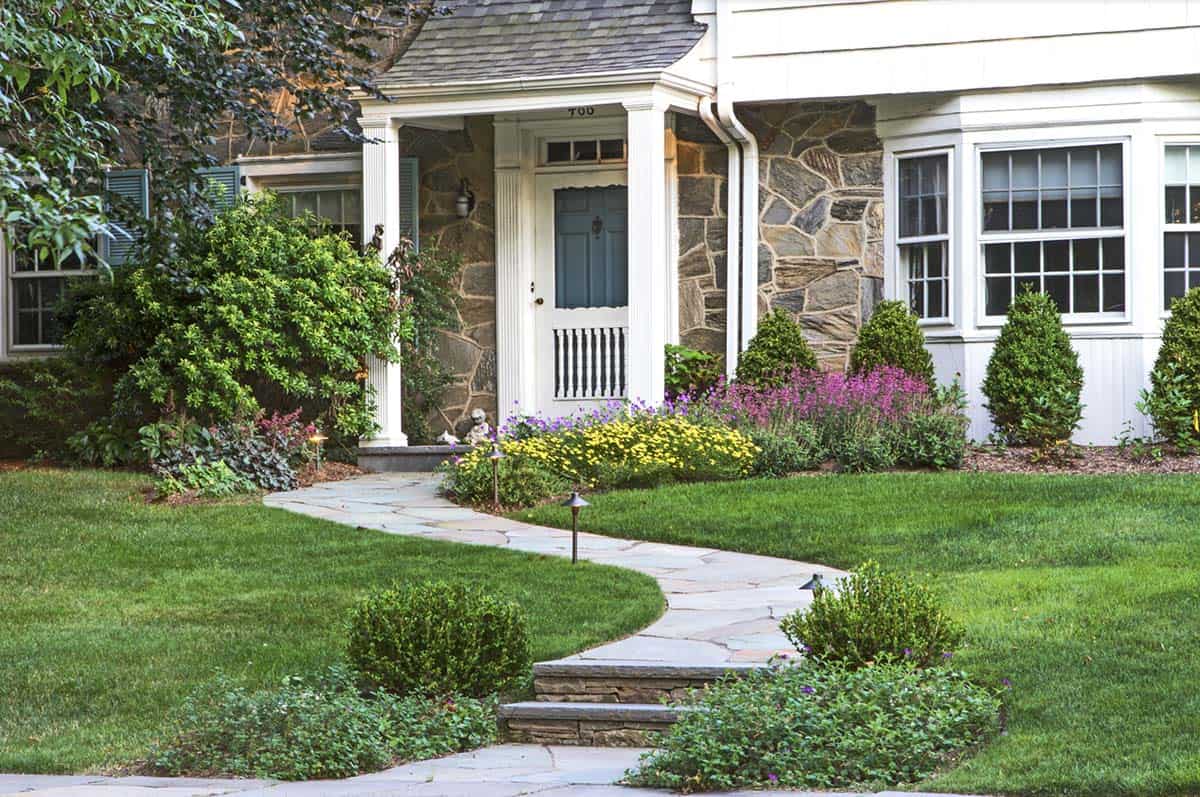 Curved bluestone walkway lined with coreopsis, geranium, and agastache leading to a stone home entry