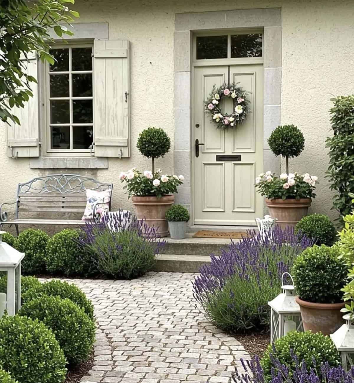 Cottage front garden with boxwood topiaries, lavender, and a cobblestone path leading to the door