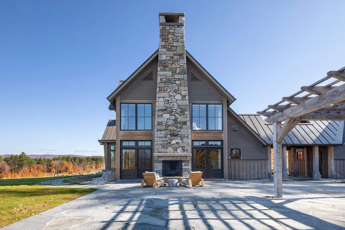 Timber-frame home exterior with stacked stone chimney and patio seating