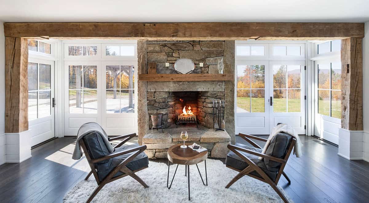Living room with stone fireplace flanked by French doors and reclaimed wood mantel beam