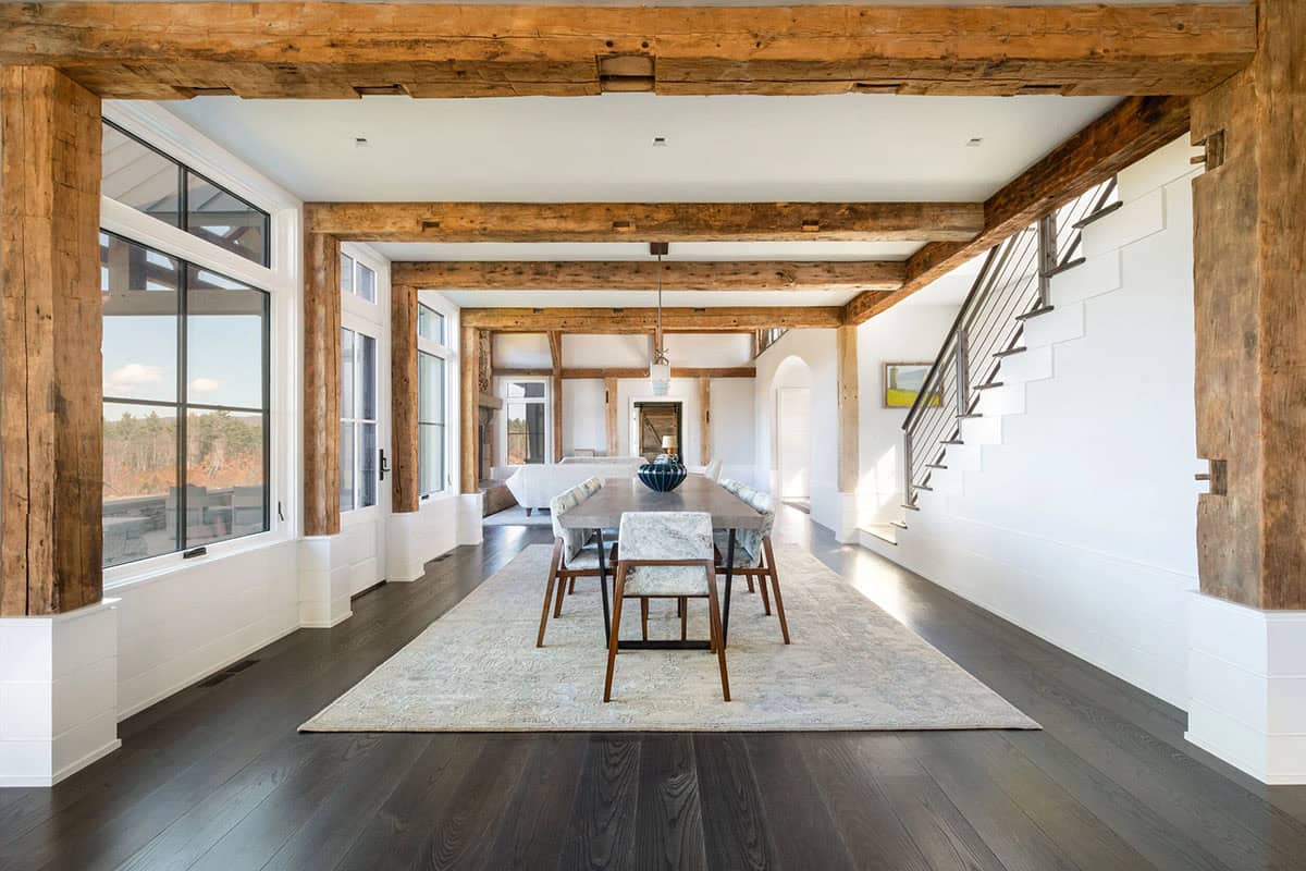 Dining area framed by reclaimed timber posts and beams with staircase view