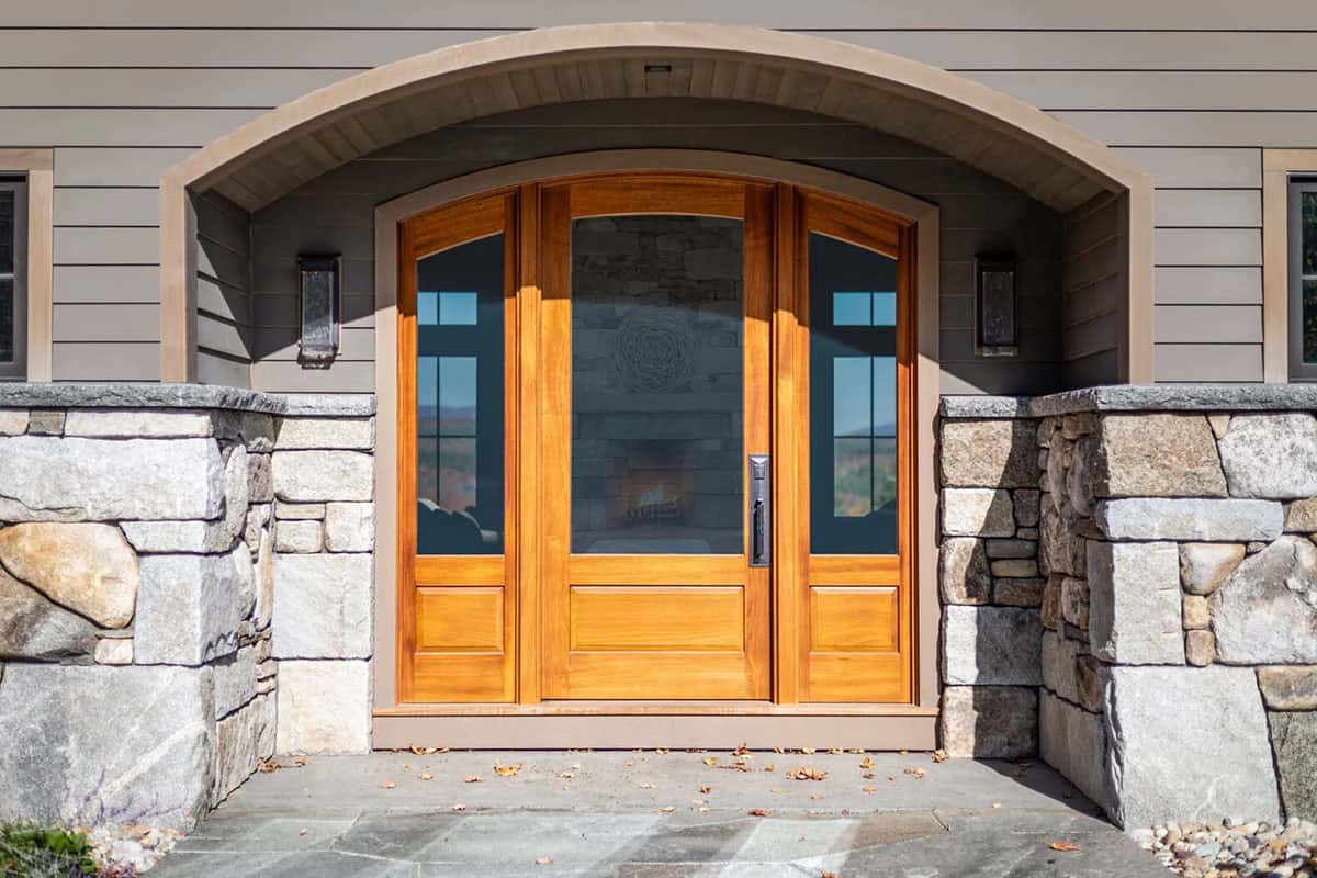Arched mahogany front door framed by stacked stone columns