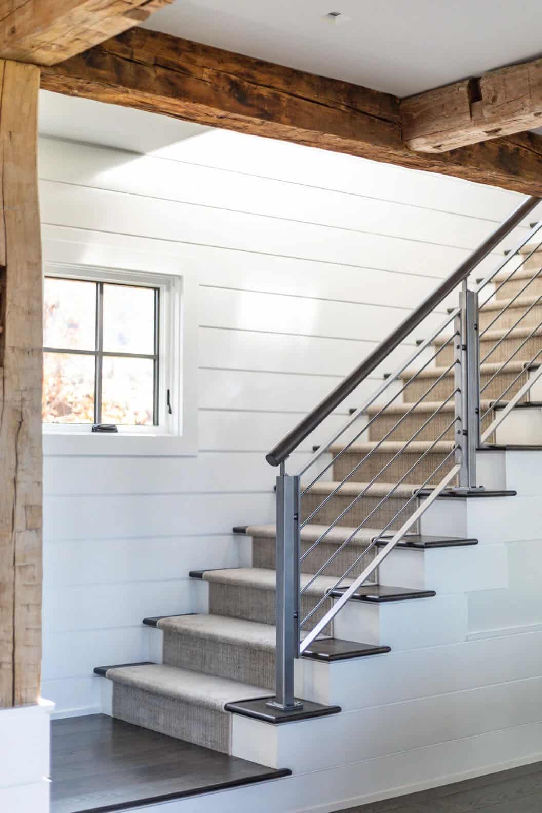 Staircase with woven stair runner and cable railing beneath reclaimed beam